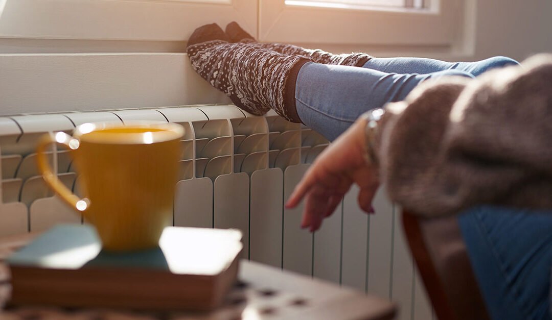 Woman heating feet on a chilly winter day, energy and gas crisis, cold room, pondering other Innovative Heating Strategies